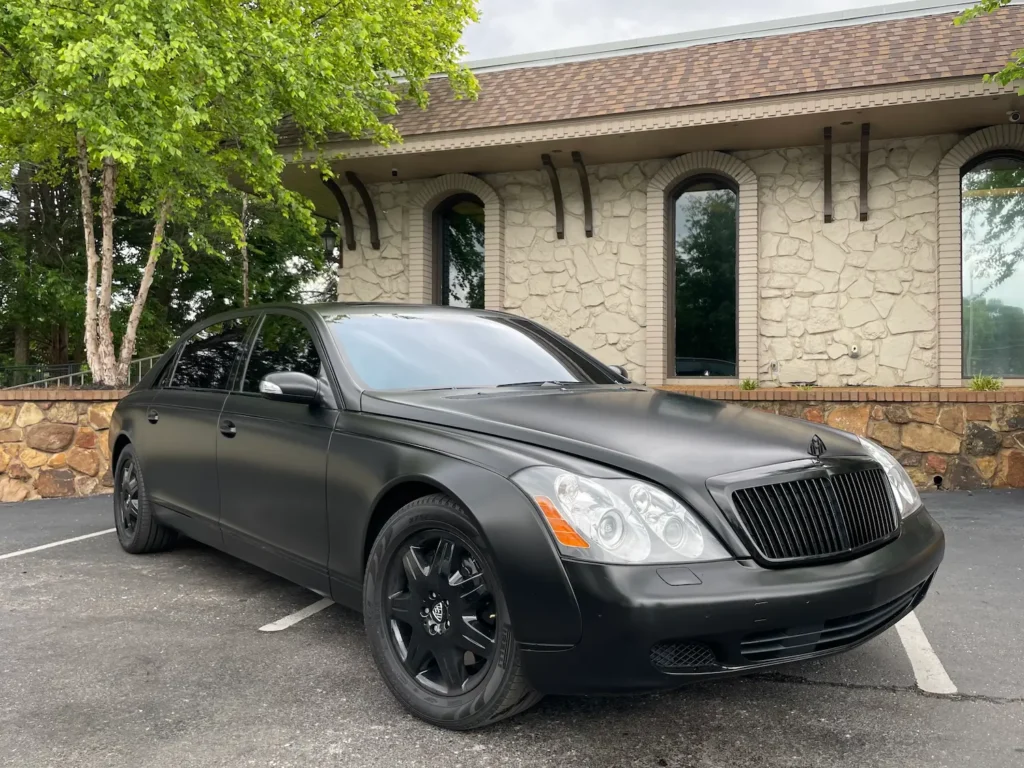 2004 Maybach 62 luxury sedan in matte black exterior, parked outside a stone-clad building.
