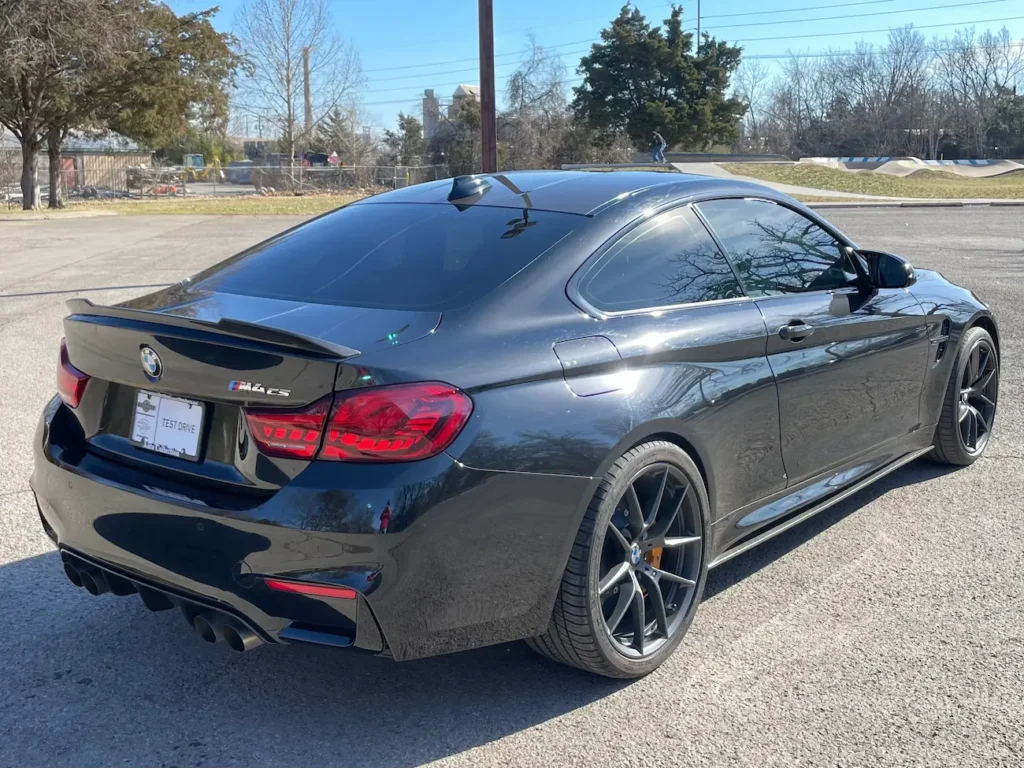 Rear view of a 2019 BMW M4 CS in black showing quad exhausts, carbon fiber spoiler, and sporty stance in daylight.