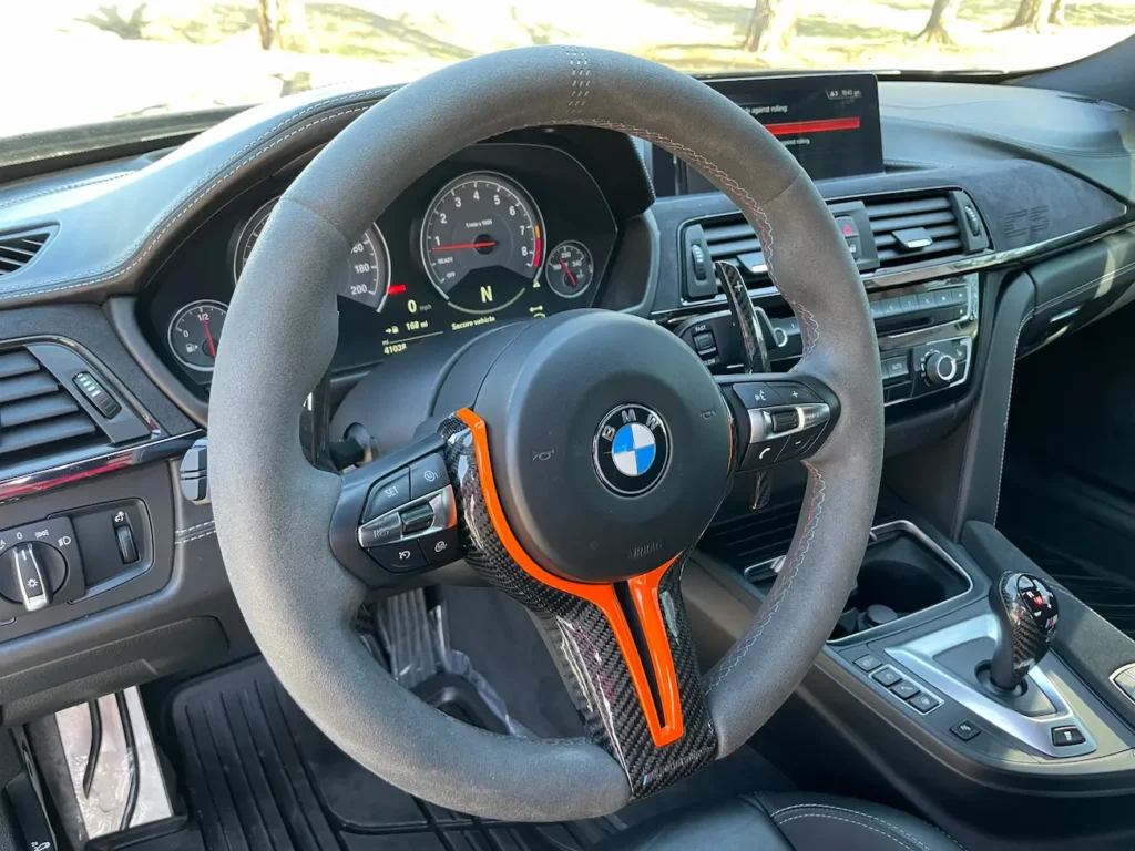 Interior of 2019 BMW M4 CS showing Alcantara steering wheel with orange stripe and carbon fiber accents.