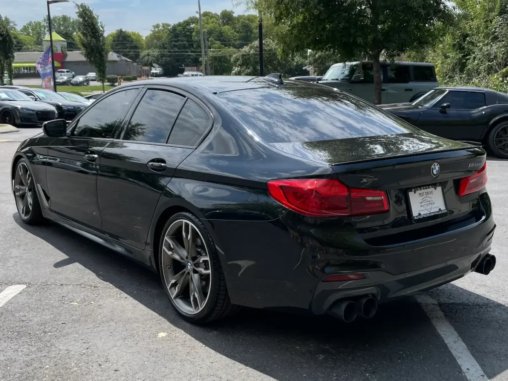 BMW M550i xDrive rear view showing LED taillights and quad exhaust system.