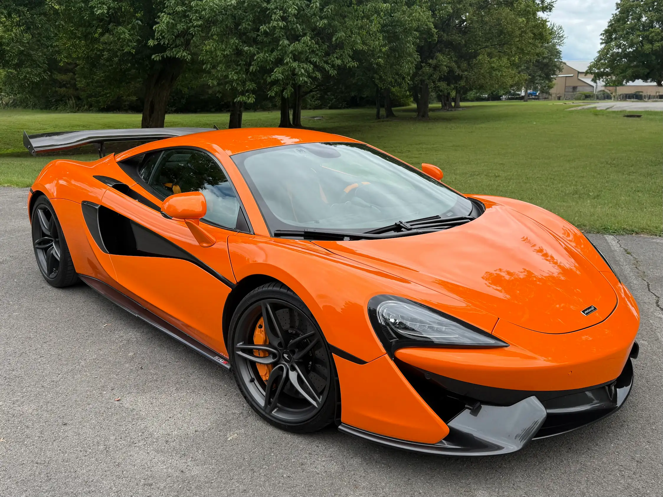 Orange 2019 McLaren 570S viewed from the front quarter, showing dark wheels, a low splitter, and a rear wing.
