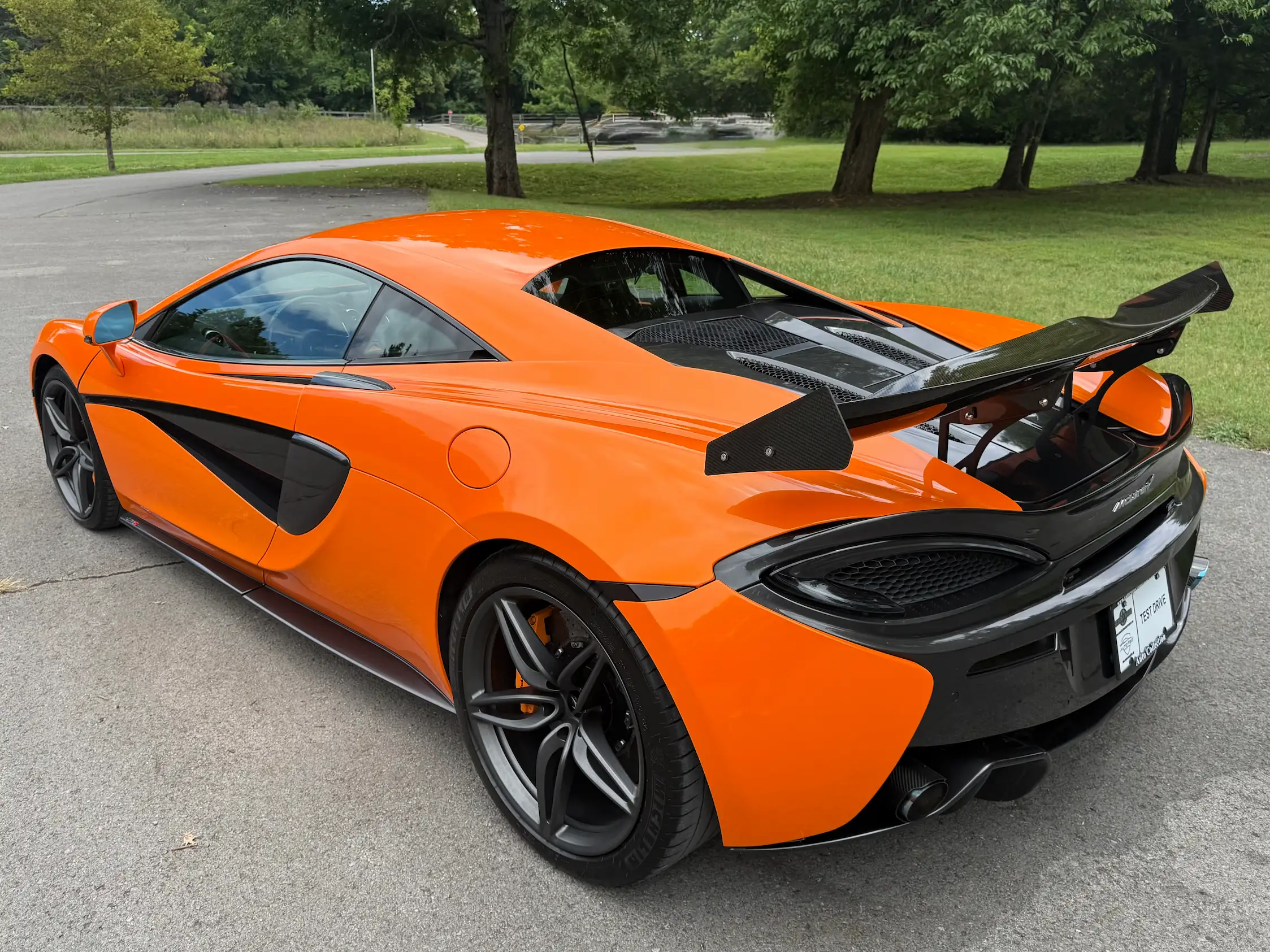 Orange 2019 McLaren 570S from the rear quarter, showing a large rear wing, dark wheels, and rear diffuser.