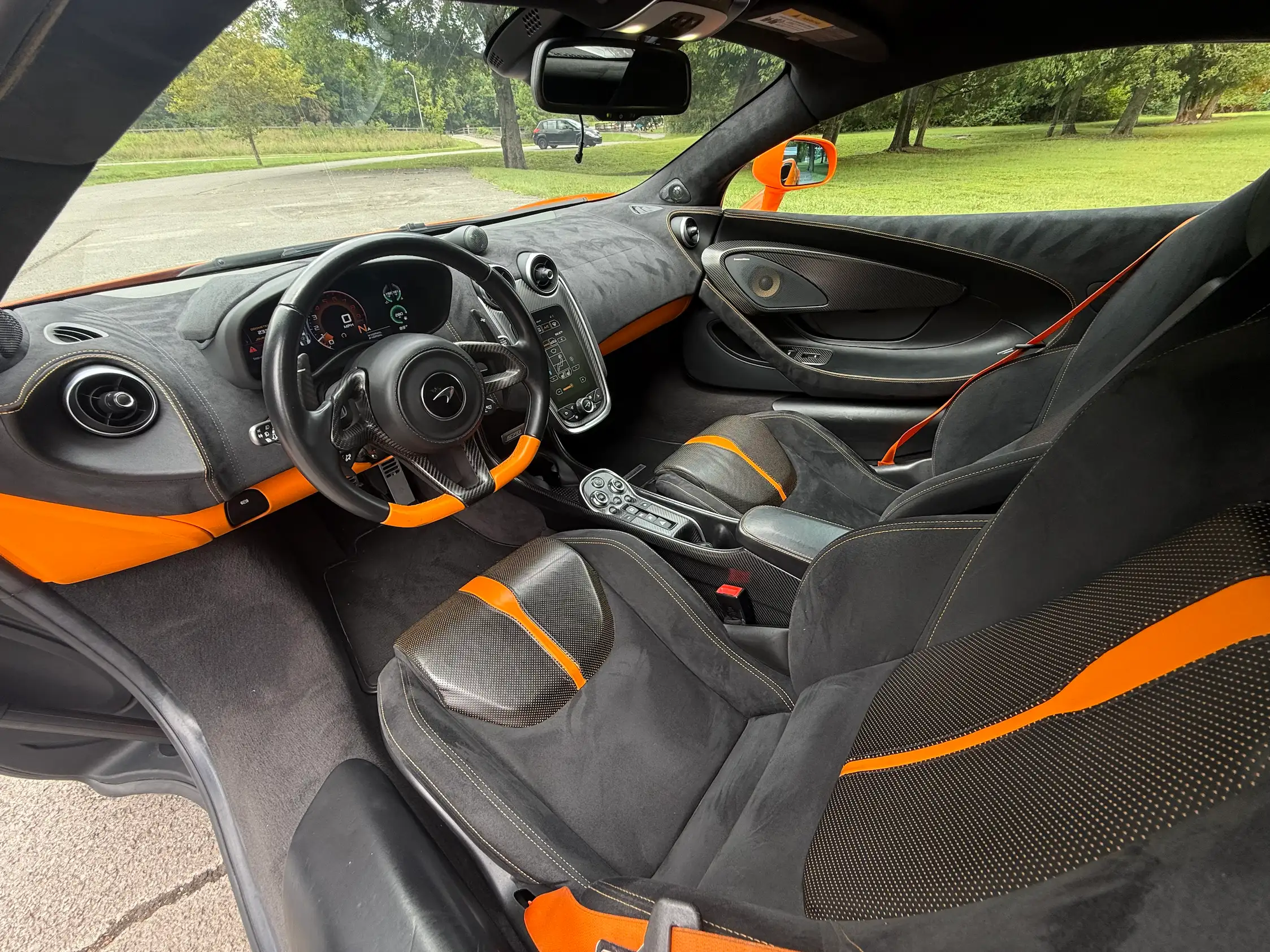 2019 McLaren 570S cabin with dark contoured seats, orange accents, a digital instrument display, and a vertical touchscreen.