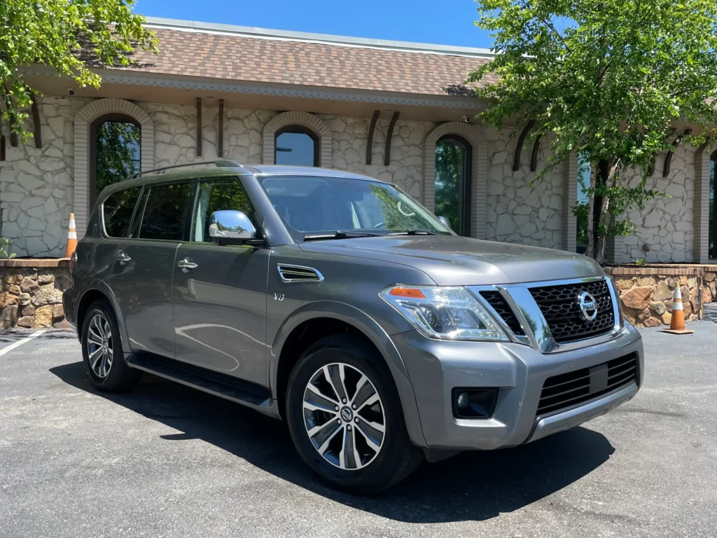 2019 Nissan Armada in gray parked outside a stone building with trees in the background.