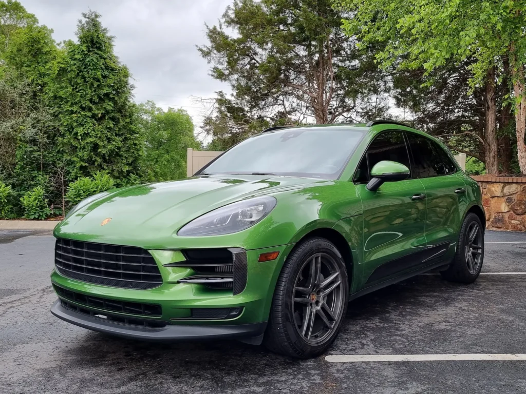 A striking green 2019 Porsche Macan parked outdoors, showcasing its sporty front view with sleek headlights and an iconic Porsche grille.