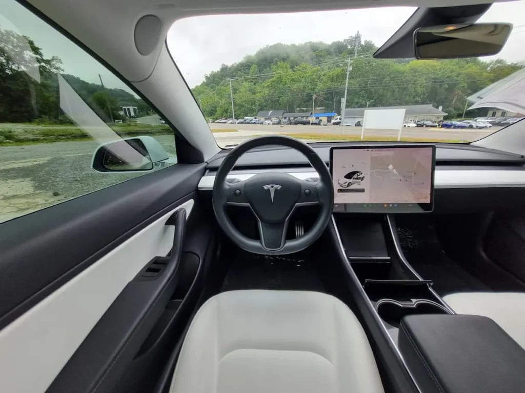 Tesla Model 3 interior view showing steering wheel and center touchscreen display with minimalist dashboard design.