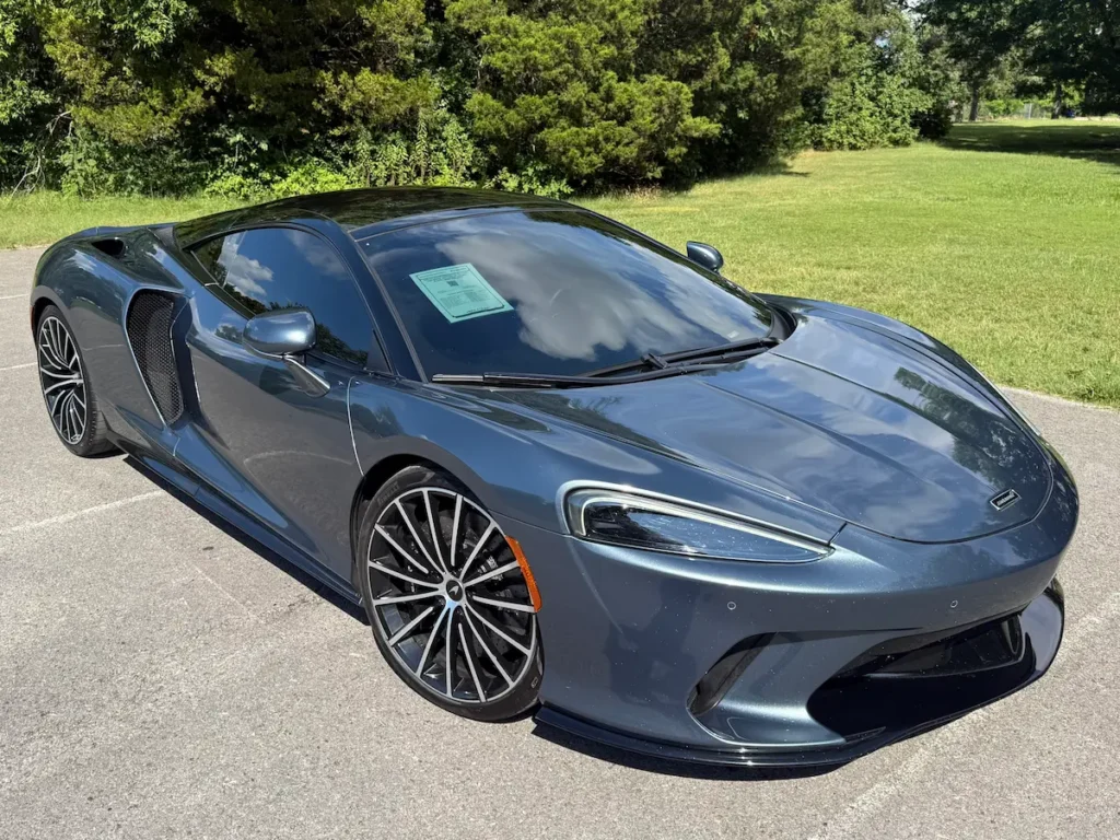 Front angle of a 2020 McLaren GT in metallic gray showing LED headlights, deep air intakes, and aerodynamic contours.