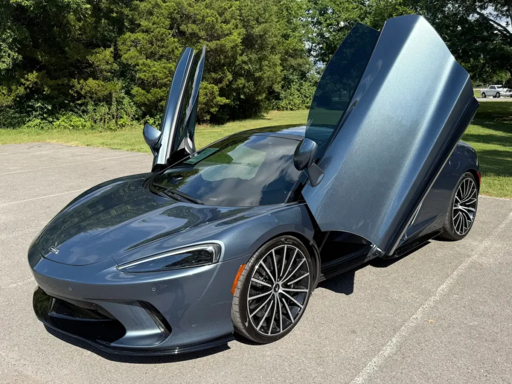 2020 McLaren GT with dihedral doors open, highlighting its sleek metallic gray finish and aerodynamic front design.