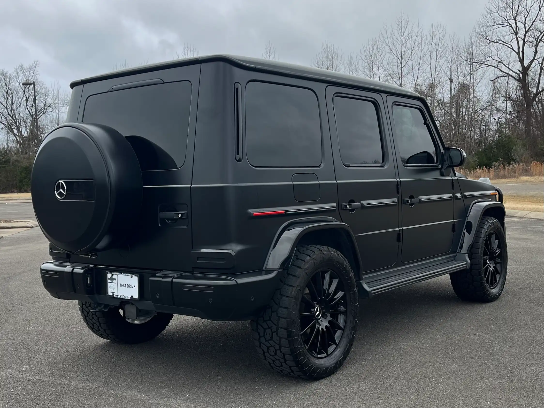 Rear three-quarter view of a black 2020 Mercedes-Benz G 550 with a rear-mounted spare wheel and side steps.