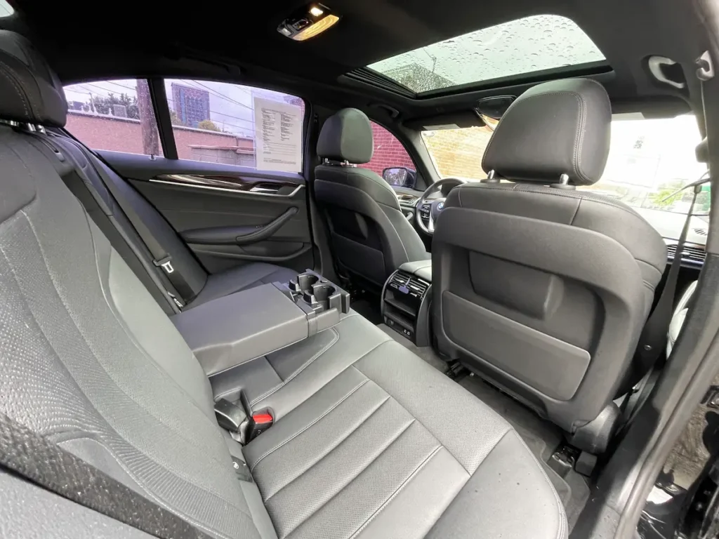 BMW 530i rear seat interior with leather upholstery, center armrest, and panoramic sunroof.