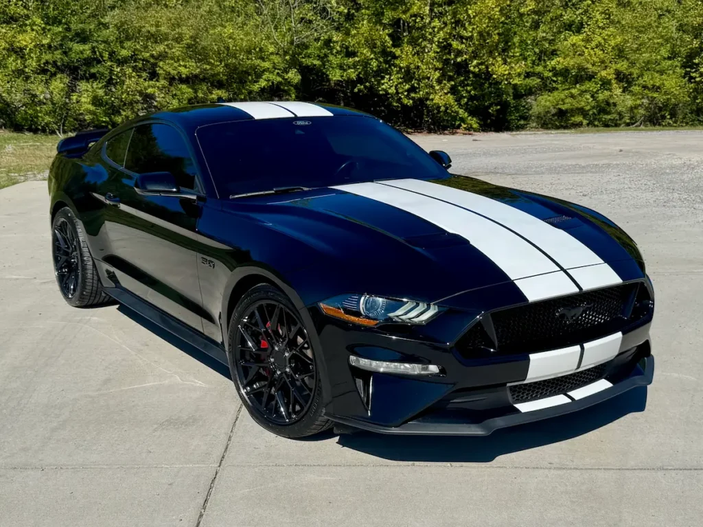 2021 Ford Mustang GT coupe in black with white racing stripes parked outdoors.