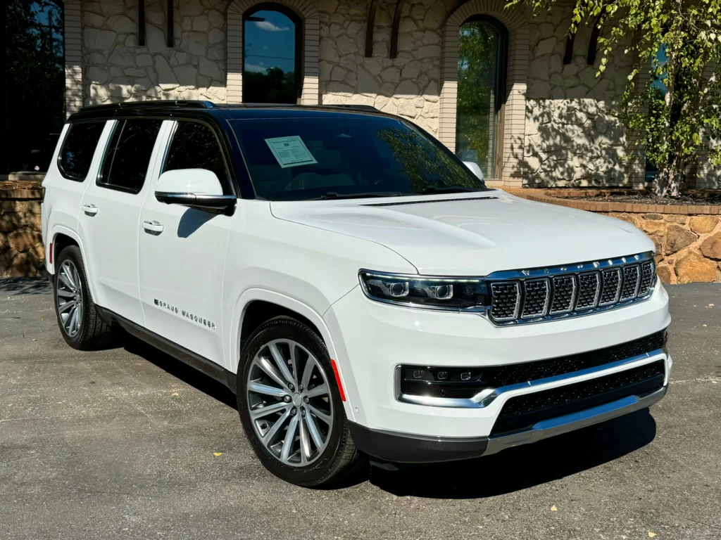 2022 Jeep Grand Wagoneer in white with bold front grille and premium alloy wheels, parked in a modern setting."