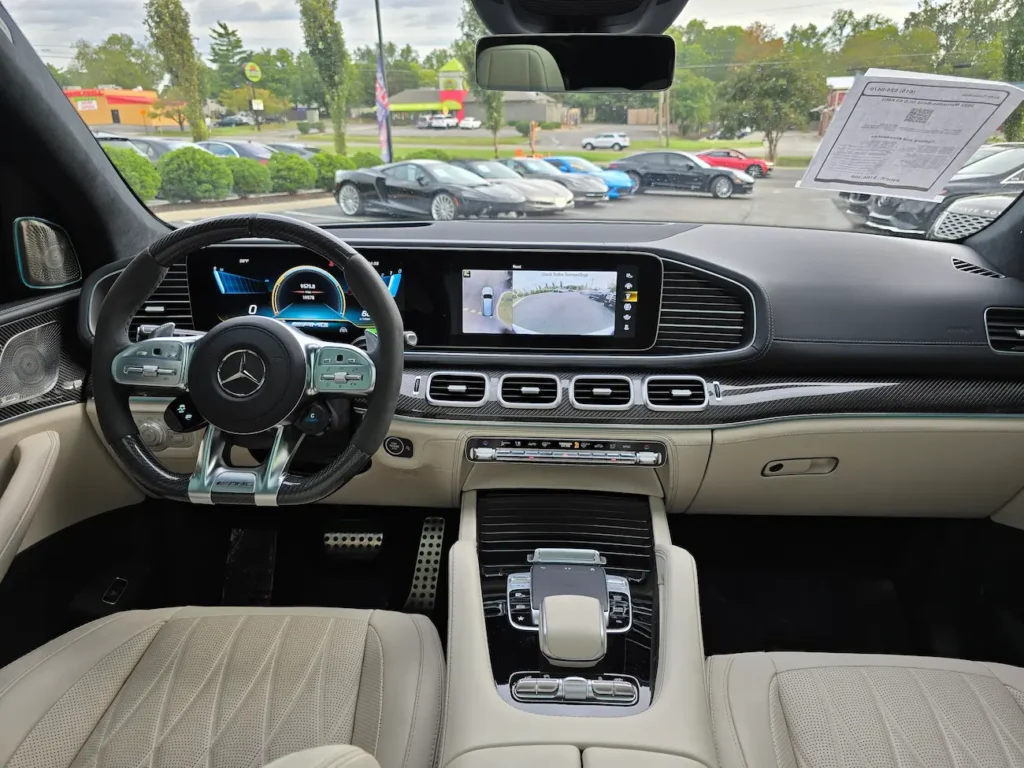 Front interior of 2022 Mercedes-Benz GLS 63 AMG with carbon-fiber trim, AMG steering wheel, and dual digital displays.