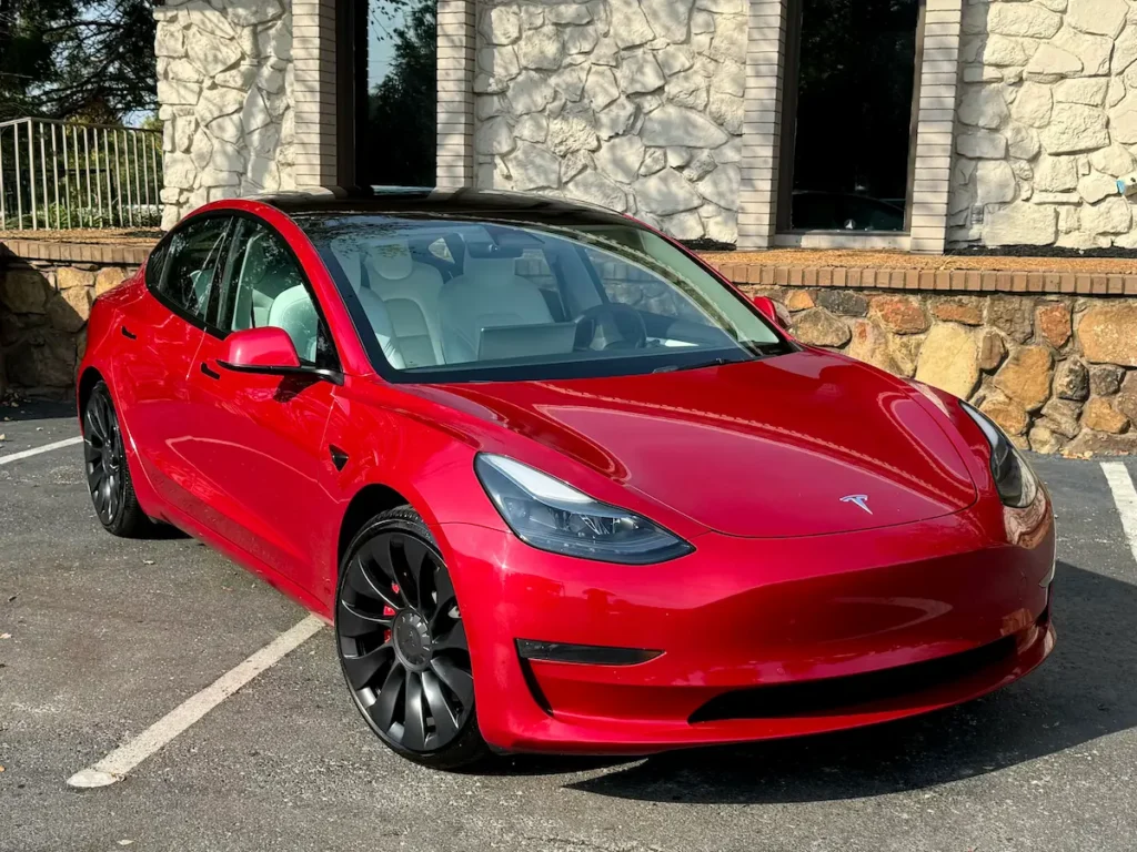 Red Tesla Model 3 Performance front three-quarter view showing sport wheels and sleek aerodynamic design.