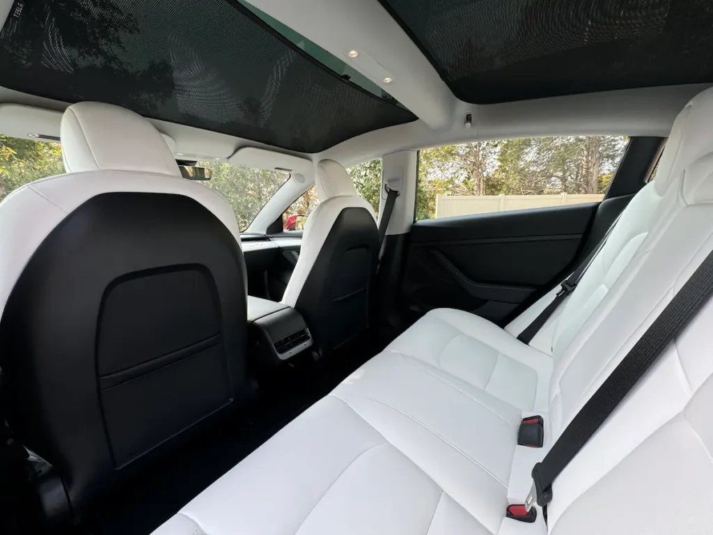 Tesla Model 3 rear seat area with white vegan leather upholstery and panoramic glass roof.