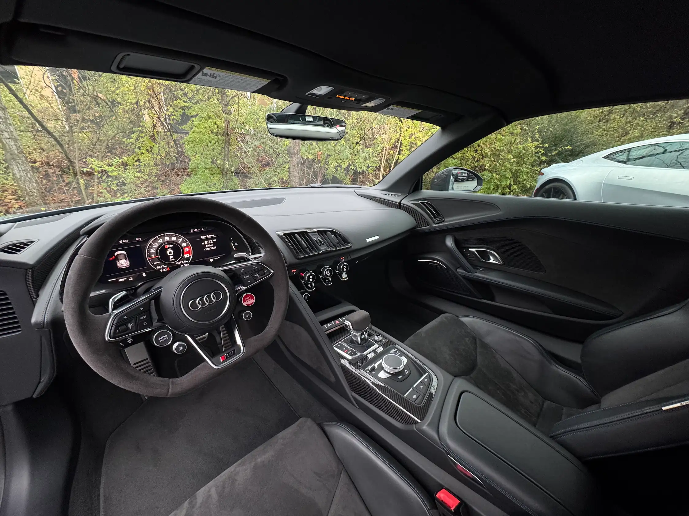 Black 2023 Audi R8 Spyder interior showing a flat-bottom steering wheel, digital gauges, gear selector, and center controls.