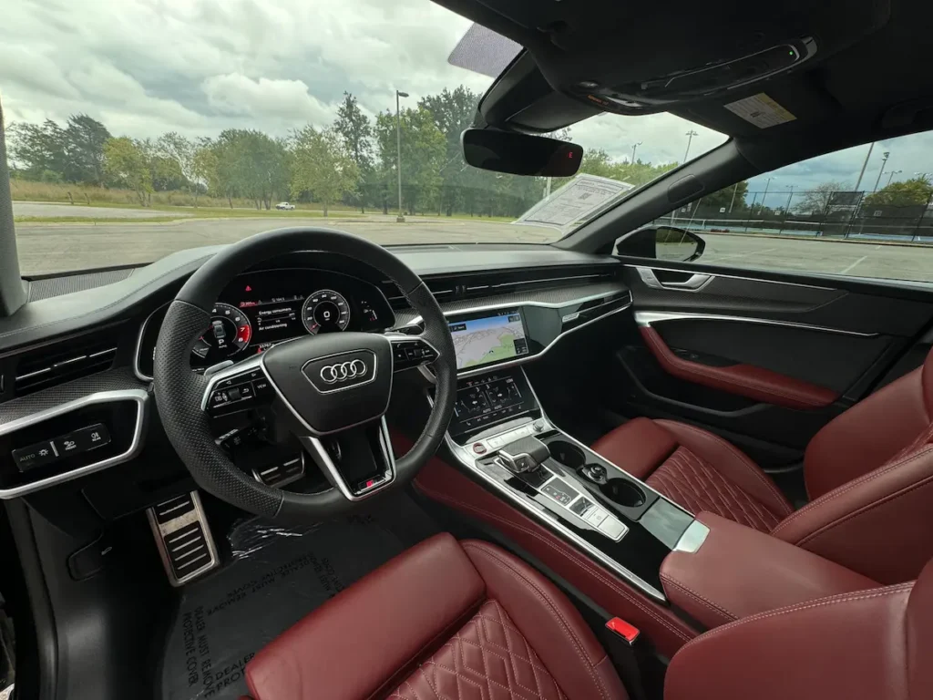 Interior of 2023 Audi S7 featuring digital cockpit, red diamond-stitched leather seats, and carbon trim.