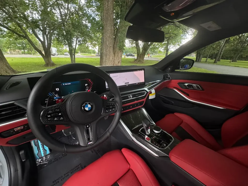 2023 BMW M3 interior with red leather seats, digital cockpit, and carbon-fiber trim.