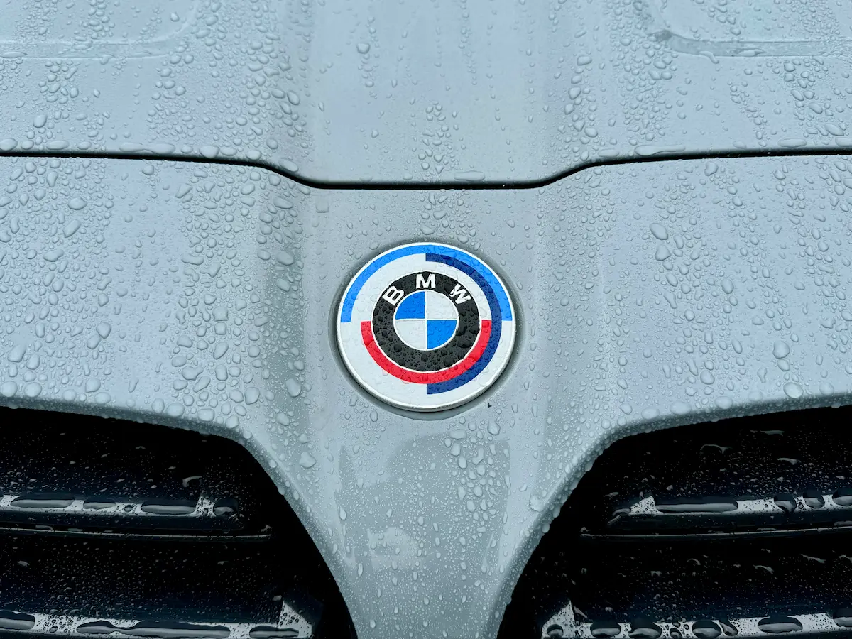BMW M badge on hood with water droplets highlighting performance branding