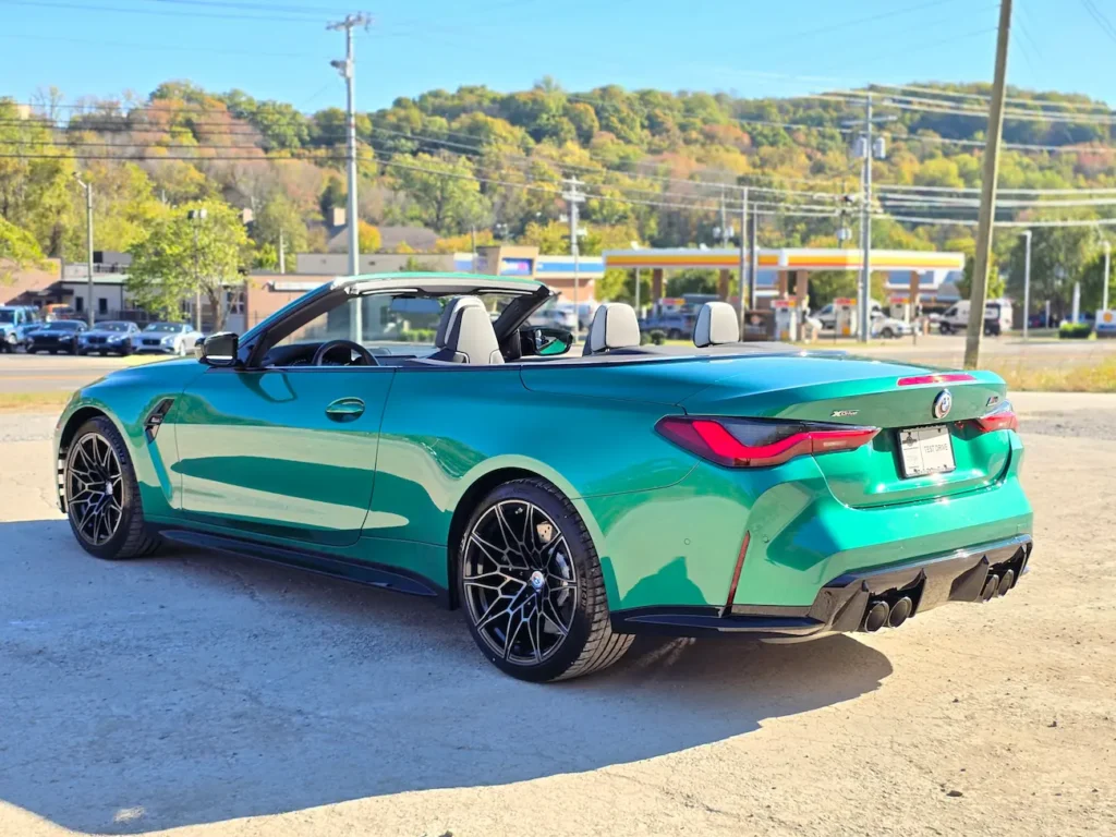 Rear three-quarter view of 2023 BMW M4 Competition Convertible in Isle of Man Green with quad exhaust and open roof.