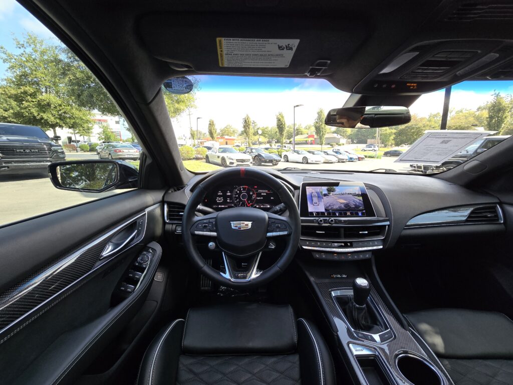 2023 Cadillac CT5-V Blackwing driver cockpit with leather-wrapped steering wheel, digital gauges, carbon trim, and manual transmission shifter.