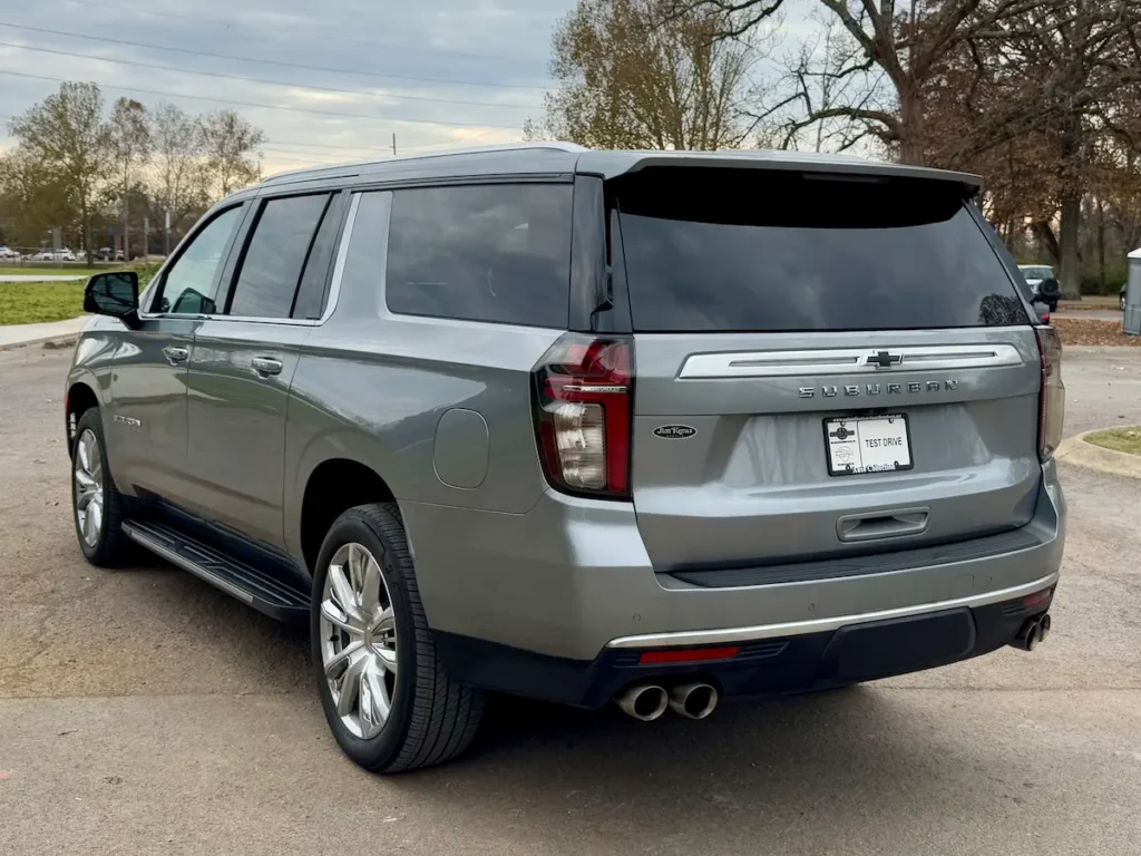 Rear and side angle of a 2023 Chevrolet Suburban High Country in metallic silver with chrome accents and quad exhaust.