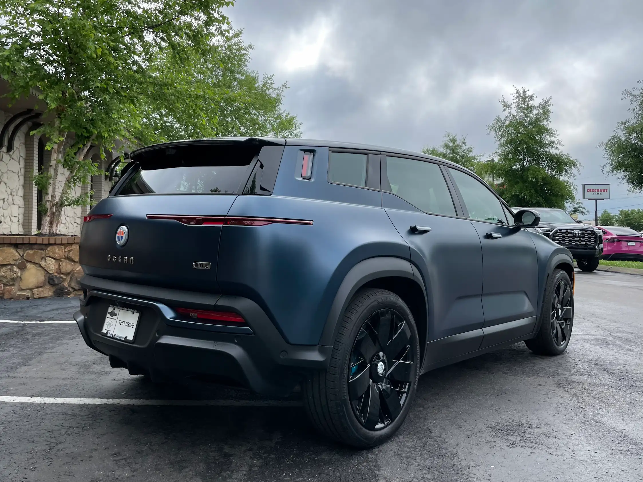 Blue 2023 Fisker Ocean One viewed from the rear three-quarter angle, showing slim taillights, black wheels and the One badge.