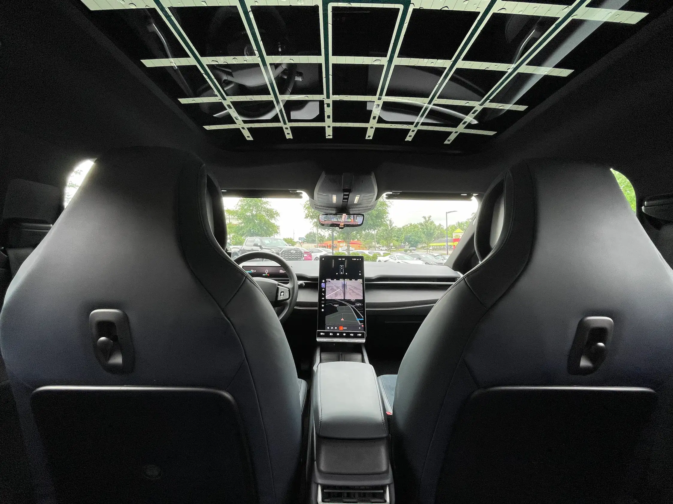 2023 Fisker Ocean One cabin viewed from the rear seats, showing black front seatbacks, a patterned glass roof and central screen.