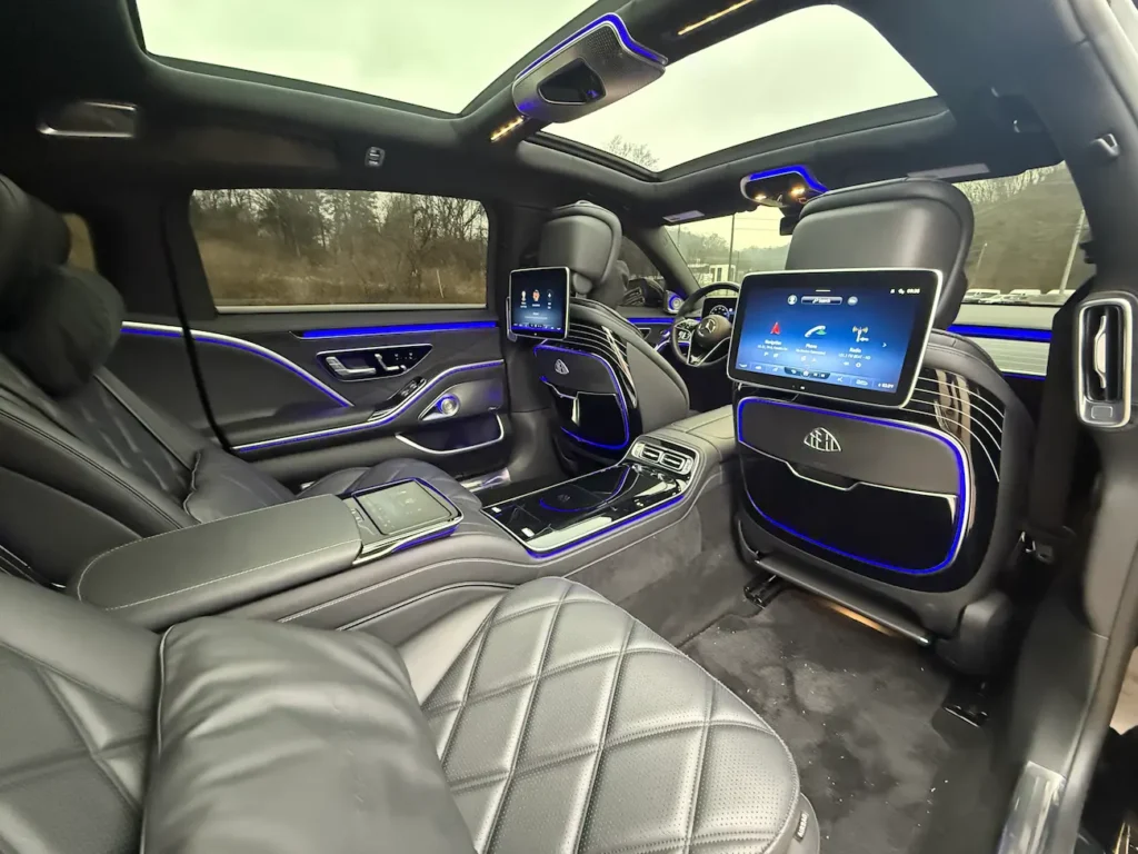 Rear interior of 2023 Mercedes-Benz S680 Maybach with reclining lounge seats, dual screens, and blue ambient lighting.