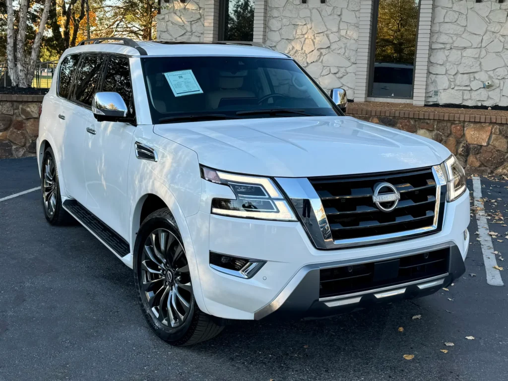 2023 Nissan Armada in white parked outside a stone building with trees in the background.
