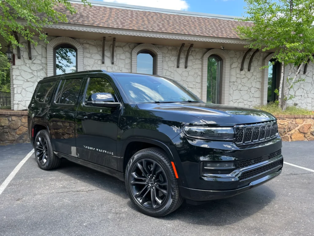 Exterior of the 2023 Black Jeep Grand Wagoneer with a sleek design, bold grille, and chrome accents parked in a scenic setting.
