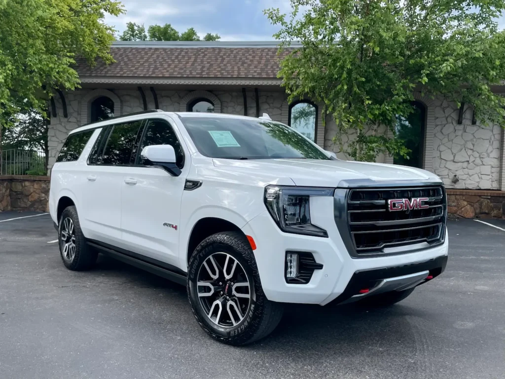 hite 2023 GMC Yukon AT4 viewed from the front side, showing bold grille, red tow hooks, and off-road stance.