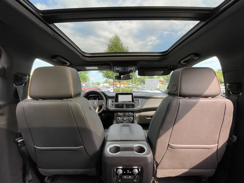 View from second-row seats inside a 2023 GMC Yukon AT4, showing the dashboard, front seats, and infotainment screen.