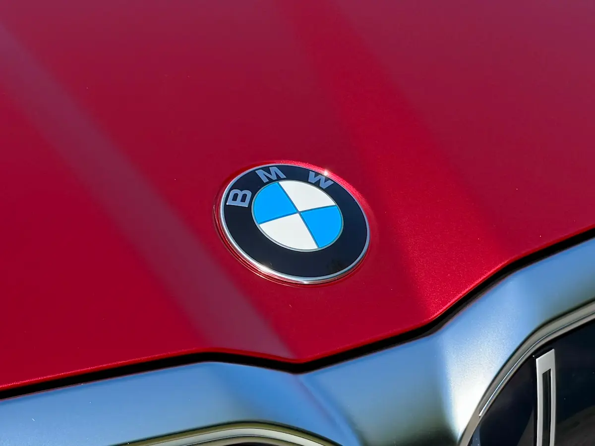 BMW 530i hood close-up with BMW roundel logo on red paint.