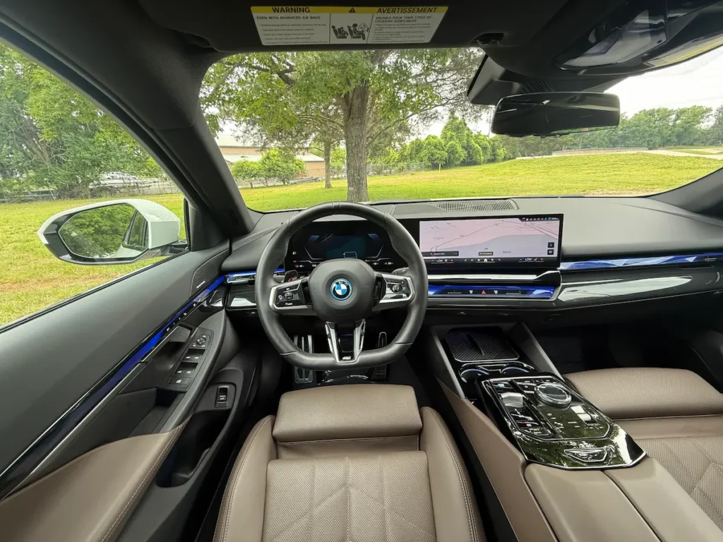 Driver’s seat view of the 2024 BMW i5 showing the steering wheel, curved display and center controls.