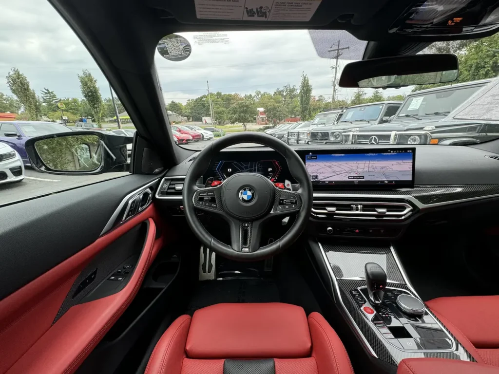 Cockpit of 2024 BMW M4 Competition showing digital display, M steering wheel, and carbon console.