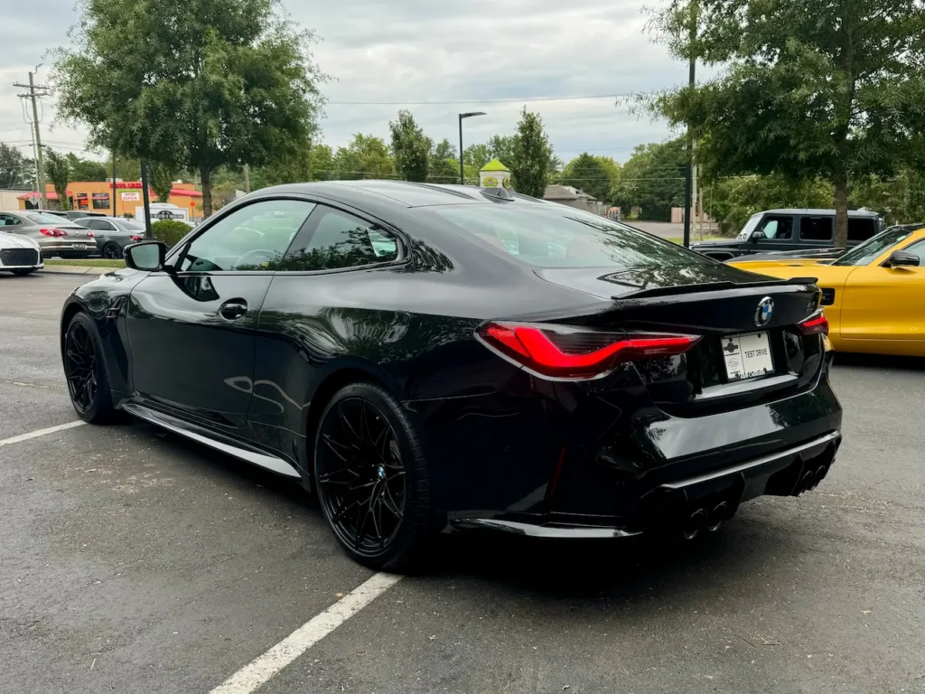 Rear three-quarter view of black 2024 BMW M4 Competition with quad exhaust and aerodynamic rear design.