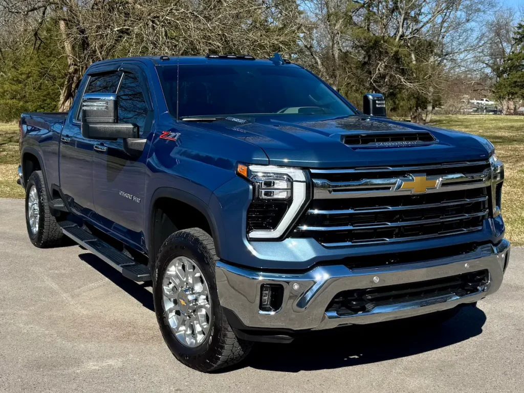 Front three-quarter angle of a blue 2024 Silverado 2500HD LTZ showing chrome grille and hood scoop.