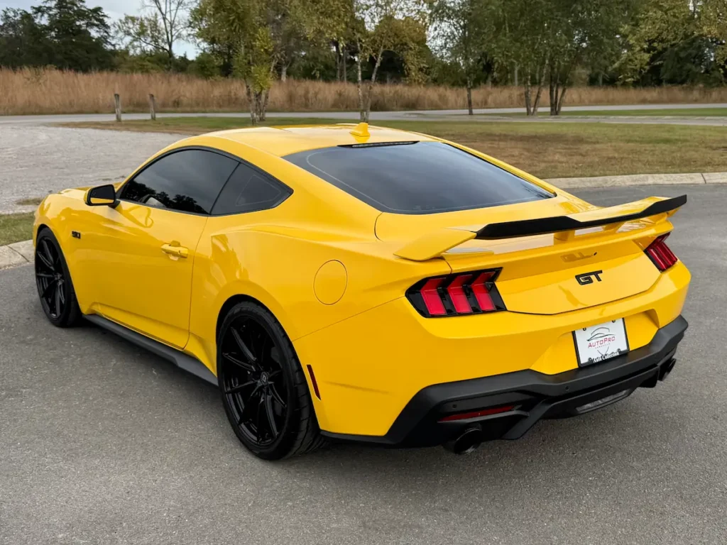 Rear three-quarter view of a yellow 2024 Ford Mustang GT Premium with spoiler.