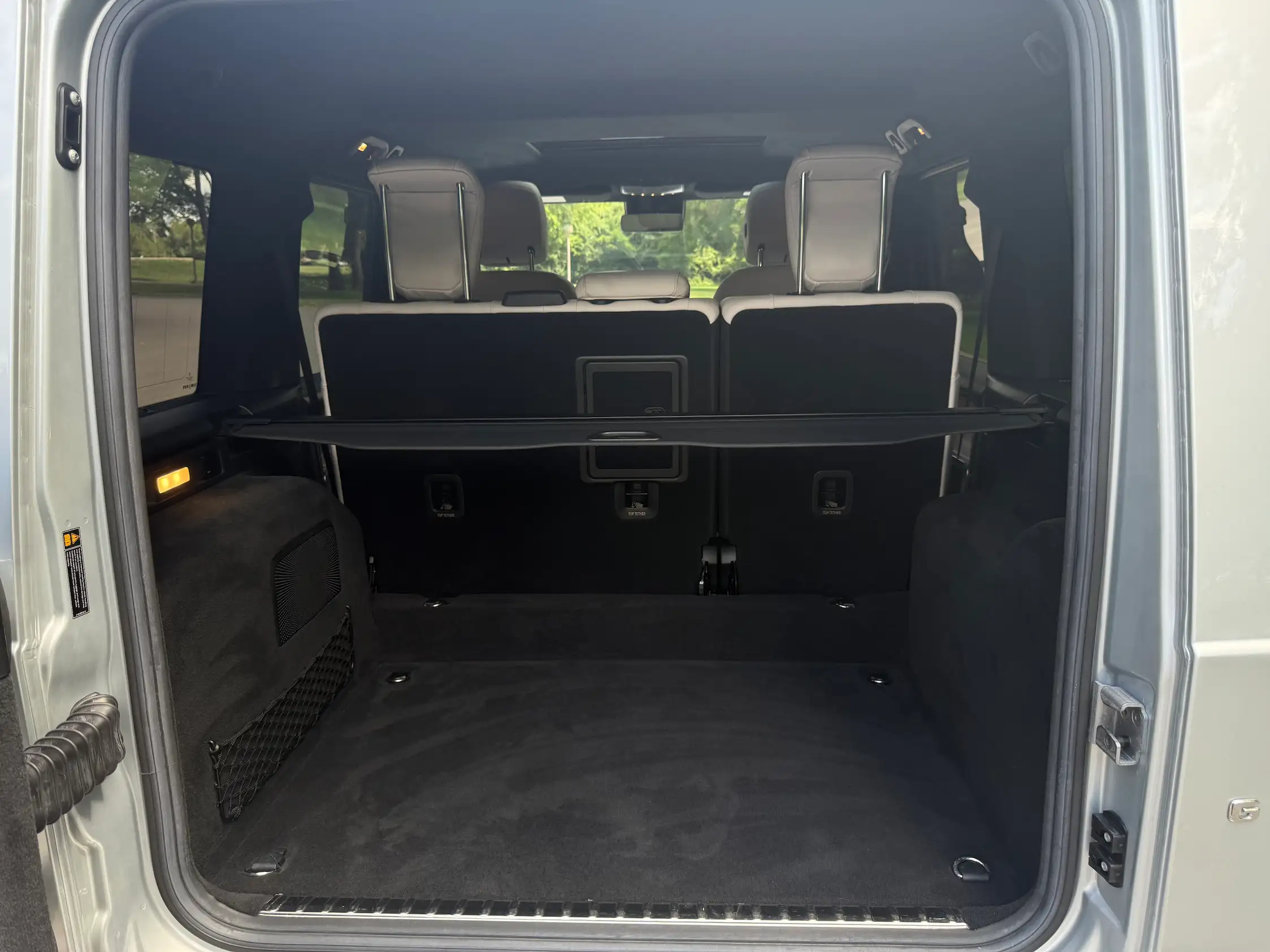 Open cargo area of a 2024 Mercedes-AMG G 63 with the rear seats upright and a retractable luggage cover.