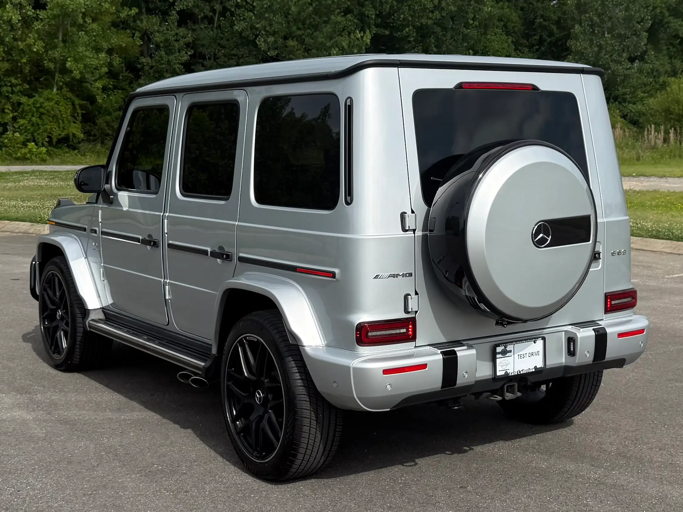 Silver 2024 Mercedes-AMG G 63 in rear three-quarter view with black wheels and a rear-mounted spare-wheel cover.