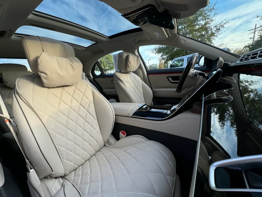 Interior front seats of the 2024 Mercedes-Benz S580 in beige leather with quilted stitching and panoramic sunroof.