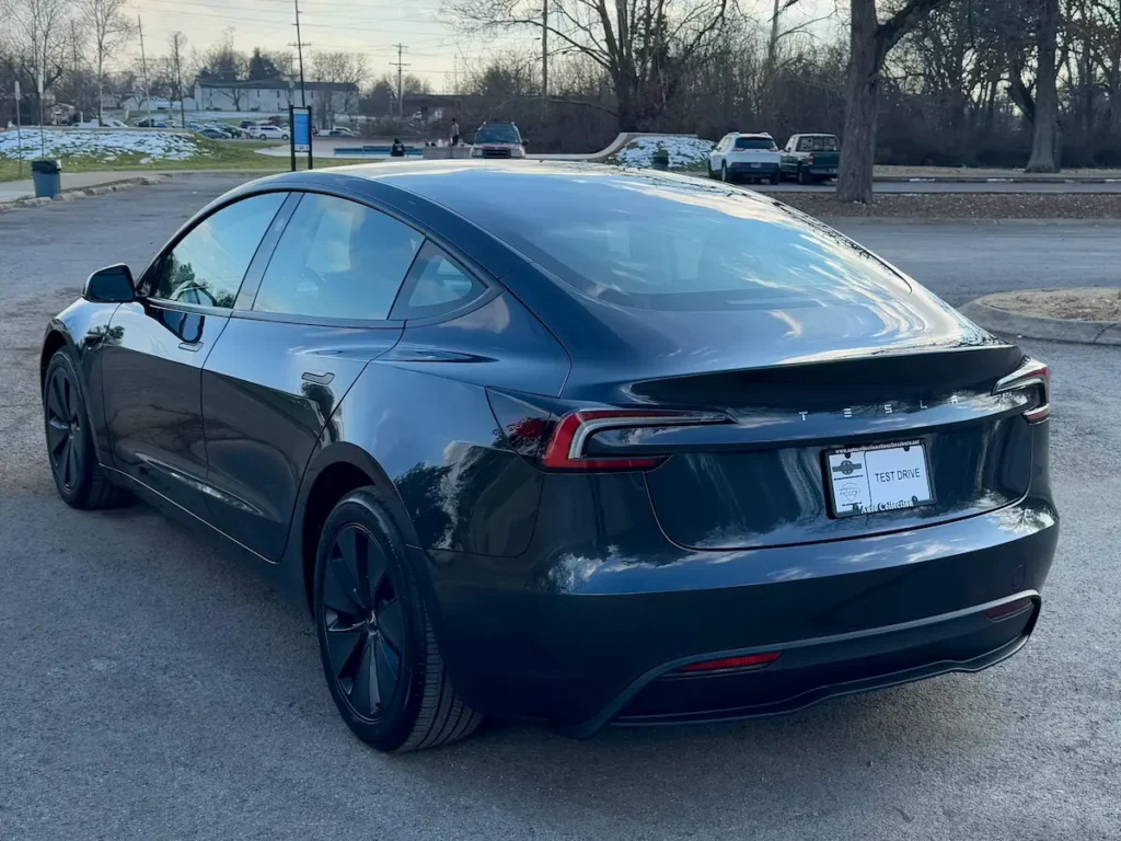 Rear three-quarter view of 2024 Tesla Model 3 Long Range in gray, showcasing taillight design and fastback roofline.
