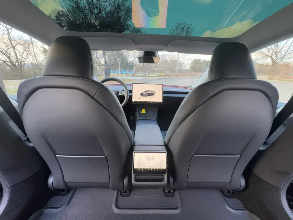 Rear-seat view of 2024 Tesla Model 3 showing black leather interior and full glass roof.