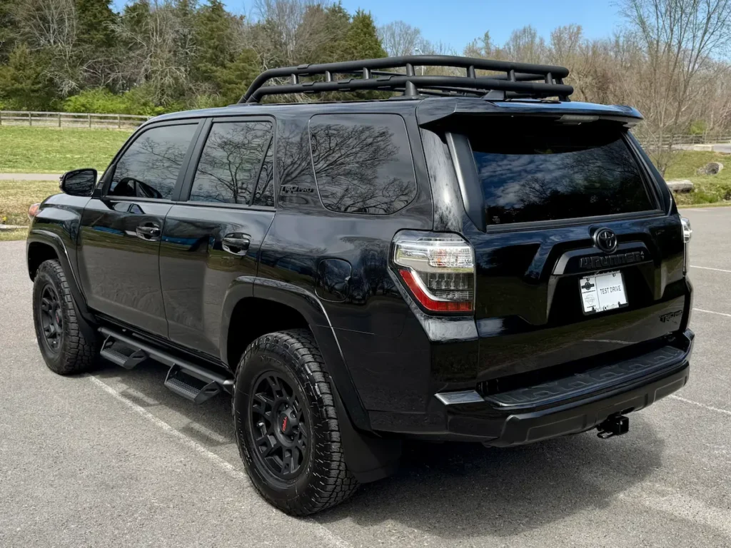Black 2024 Toyota 4Runner shown from the rear three-quarter angle with roof rack and tow hitch.