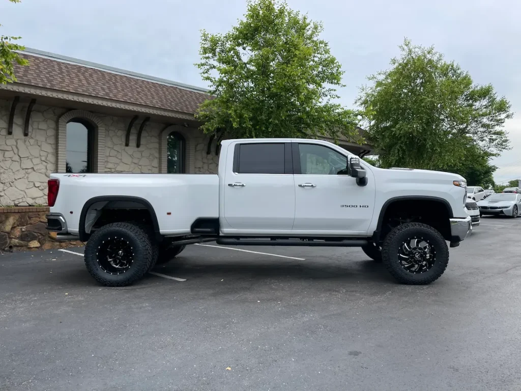 Full side profile of a lifted 2024 Silverado 3500HD LTZ dually in white with custom wheels.