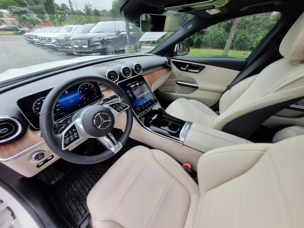 Front interior of a 2024 Mercedes-Benz C 300 Sedan with digital MBUX touchscreen and luxury wood trim.