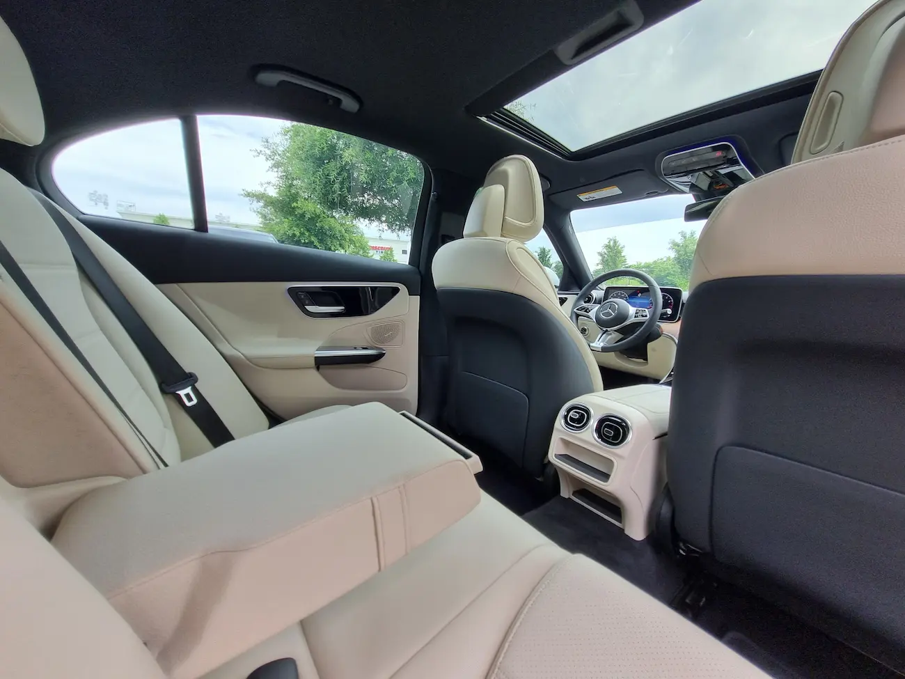 Rear passenger area of a 2024 Mercedes-Benz C 300 with beige leather seats and panoramic sunroof.