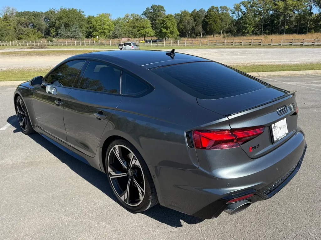 2025 Audi RS5 Sportback in gray viewed from the rear showcasing LED taillights and quad exhaust tips.