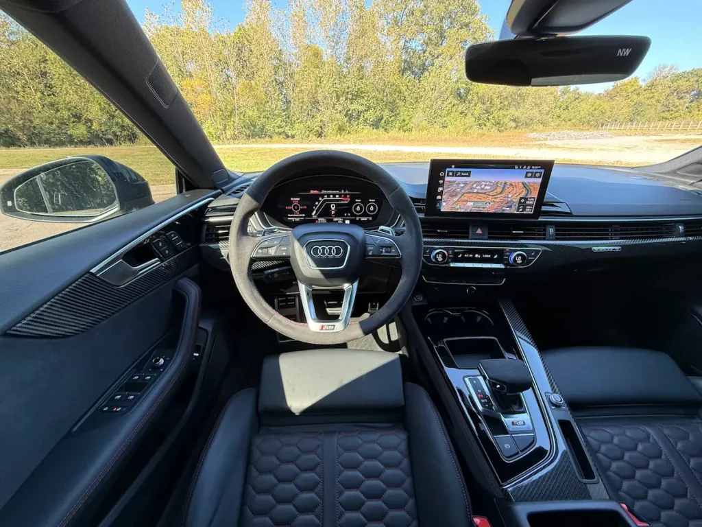 Interior of 2025 Audi RS5 featuring digital cockpit, flat-bottom steering wheel, and carbon-fiber trim.